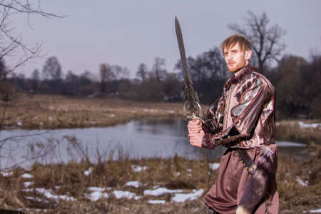 Costume Play. Warrior wirh Sword Posing in Fighting in Front of River Outdoors. Horizontal imageの写真素材