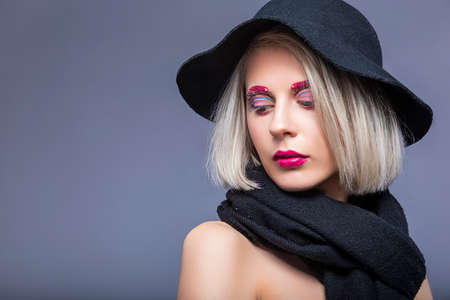 Portrait of Beautiful Caucasian Blond Girl in Black Hat Over Gray Background with Facial Make-Up....