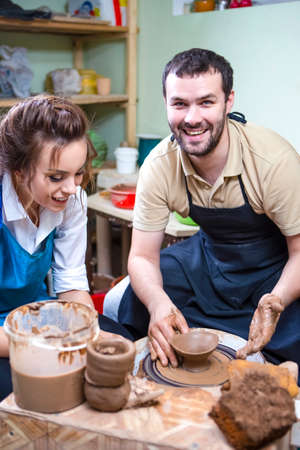 Experienced Male Potter Tutor Working with Female Apprentice with Clay Lump on Potter's Wheel in...