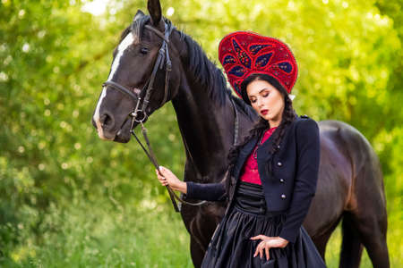 Fashion Caucasian Model in Kokoshnik Posing With Thoroughbred Horse Against Nature Background...