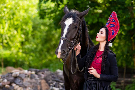 Lovely Fashion Model in Russian Style Kokoshnik Holding Thoroughbred Horse Closely.Posing Against Nature Background. Horizontal Imageの写真素材