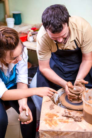 Experienced Male Potter Tutor Working with Female Apprentice with Clay Lump on Potter's Wheel in...