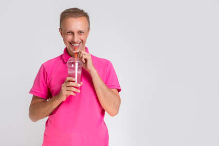 Portrait of Happy Smiling Caucasan Blond Man Holding Cup With Smoothie. Drinking Through Straw. Horizontal Imageの写真素材
