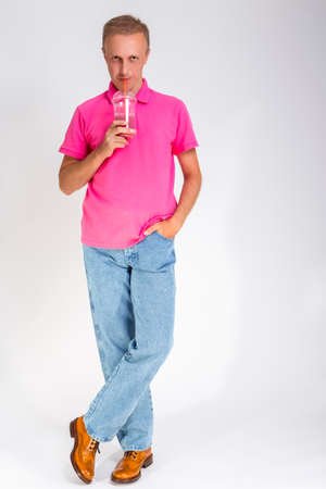 Full Length Portrait of Smiling Caucasan Blond Man Holding Cup With Smoothie. Drinking Through Straw. Vertical Imageの写真素材