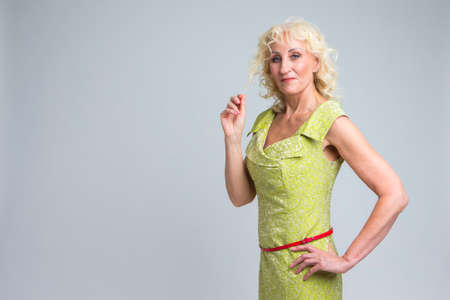 Happy Mature Caucasian Blond Woman Posing in Green Dress Indoors.  Horizontal Image Orientationの写真素材
