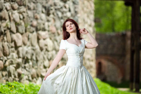 Dreaming Young Lady in White Dress and Red hair. Posing Against Ancient Castle. Horizontal Shotの写真素材