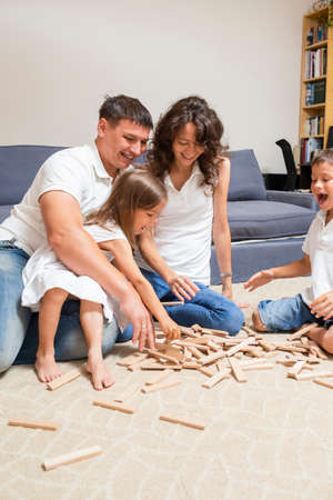 Portrait of Four Family Members Working Together. Making Wooden Construction While Sitting On Floor Indoors. Vertical Image Orientationの写真素材