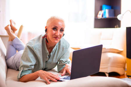 Adults and Technologies Concepts. Positive  Caucasian Senior Woman Posing with Laptop and Headphones...
