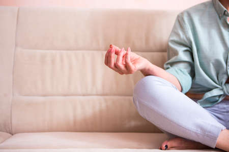 Closeup of Hands and Feet of Senior Woman Posing in Yoga Asana Pose on Couch indoors. Sitting  with...