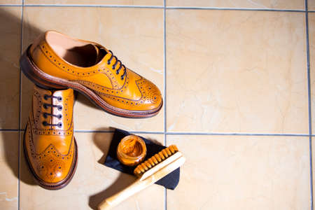 Pair of Luxury Male Full Brogued Tan Oxford Shoes. Placed Together with Shoe wax and Brush on Tiles Floor. Horizontal Image Composirionの写真素材