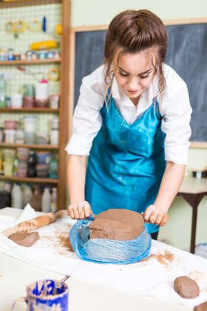 Pottering Ideas and Concepts. Smiling Female Professional Worker Preparing a Piece of Clay Using Special Wire in Professional Workshop.Vertical Image Compositionの写真素材