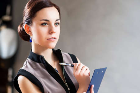 Thinking Caucasian Businesswoman with Notepad Posing with Thoughtful Expression in Studio Environment. Horizontal Image Compositionの写真素材