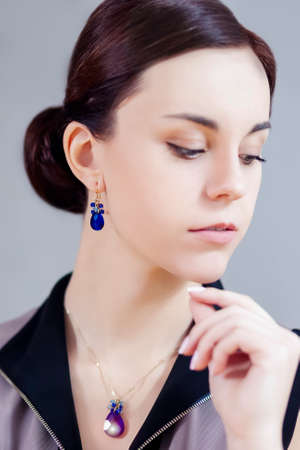 Closeup Portrait of Beautiful Caucasian Lady with Blue Pendant and Earring. Against Gray. Vertical...
