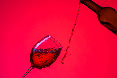 Drinks Concepts. Wine Pouring Out of Bottle On The Right Hand Side to Whineglass with Colorful Liquid, Droplets and Drops. Horizontal Shotの写真素材
