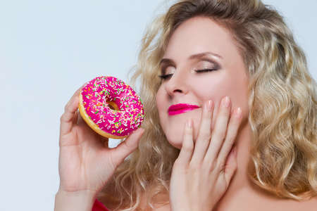 Food Concepts. Young Caucasian Blond Girl Enjoying Pink Doughnut in Hands. Posing Against White.Horizontal Imageの写真素材
