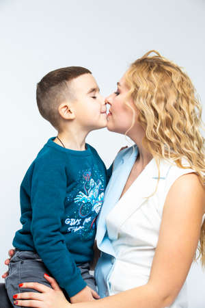 Portrait of Kissing Caucasian Mother With Her Son in Studio Indoors. Posing Against White Background. Vertical imageの写真素材