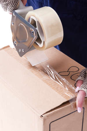 Postal and Moving. Closeup of Female Hands Packing Cardboard Box Indoors Unsing A Tape-Machine....