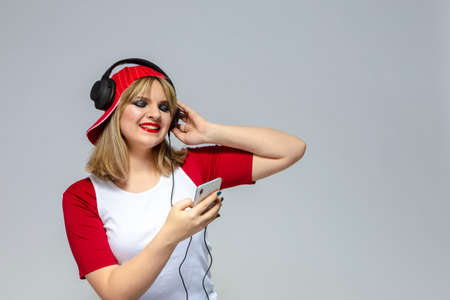 Happy Caucasian Female Blond Girl In Casual Closing Listeining To Music in Headphones On Smartphone....