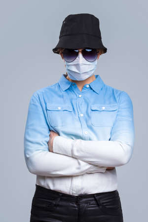 Virus Ideas. Concept of Coronavirus of Depressed Caucasian Woman In Glasses And Black Hat Wearing Flu Virus Mask For Viral Prevention. Against Gray. Vertical Shotの写真素材
