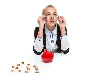 Financial Ideas and Concepts. Portrait of Thoughtful Caucasian Teenager Girl Posing With Coins and Piggy Bank. Looking Up Through Glasses. Horizontal Image Compositionの写真素材