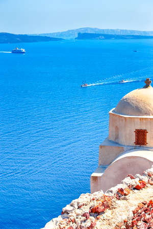 Sailing Boats Near Caldera Volcanic Slopes of Santorini Oia or Ia Village in Greece. With Traditional Pale Dome Orthodox Greek Church in Foregound.Vertical Imageの写真素材