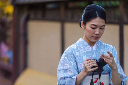 KYOTO, JAPAN - NOVEMBER, 8, 2019: Beautiful Tranquil Japanese Girl Posing in Geisha Kimono With Photocamera in Kyoto Streets, Japan.のeditorial素材