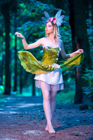 Sexy Beautiful Caucasian Female in Green Dress Decorated With Flowers Posing in Forest Outdoor.の写真素材