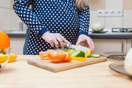 Closeup of Hands of Pregnant Woman Preparing Salad with Vegetables on Kitchen. Horizontal Compositionの写真素材