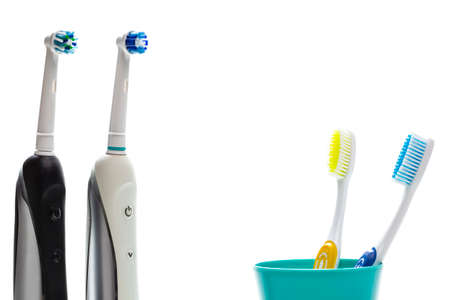 Closeup of Two Professional Electric Toothbrushes In Front of Two Manual Tooth Brushes in One Cup On White Background. Horizontal Imageの写真素材
