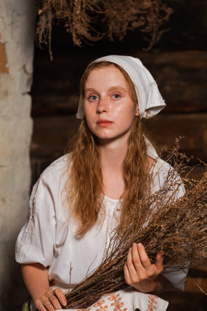 Young Beautiful Caucasian Redhaired Girl in Rustic Style Dress Posing With Heather Bouquet in Old Village House. Vertical Imageの写真素材