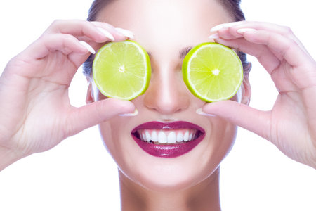 Dentistry Concept and Ideas. Portrait of Caucasian Woman with Perfect White Smile Posing With Green Lime Against Her Eyes On White Background. Horizontal Imageの写真素材