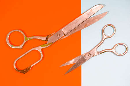 Pair of Old Rusty Tailor Scissors Placed Over Pink And Yellow Paper Background. Horizontal Image