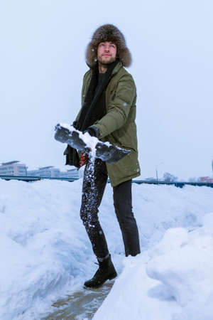 Portrait of Caucasian Handsome Man in Winter Outfit Throwing Away Snow With Shovel In City Environment. Vertical Imageの写真素材