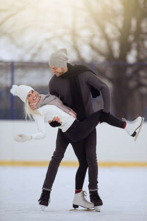 Young Caucasian Couple in Winter With Ice Skates Skating and Posing Together Over a Snowy Winter Landscape Outdoors.の写真素材