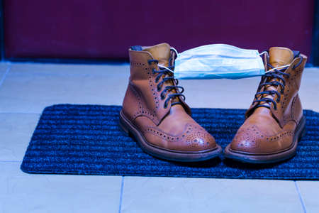 Pair of Mens Leather Tanned Brogue High Boots Covered With Facial Medical Mask as a Virus Protection Symbol. Horizontal Image Compositionの写真素材