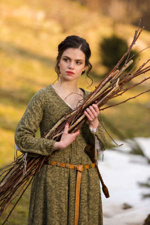 Natural Portrait of Young Brunette Girl Posing With Armful of Brushwood in Retro Dress Outdoors In Countryside Environment.Vertical Imageの写真素材