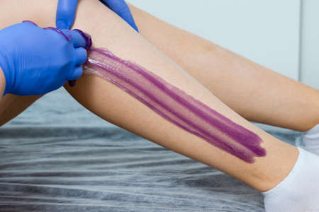 Closeup of Beautician Hands Accomplishing Woman Legs Depilation By Using Sugaring Technique on Female Legs in Salon. Horizontal Imageの写真素材
