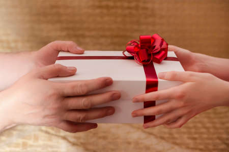 Closeup of Mature Woman Wrinkled Hands Holding and Offering Wrapped Gift Box to the Hands of Young Girl. Horizontal imageの写真素材