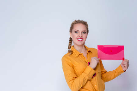 Natural Portrait  of Caucasian Blond Girl in Yellow Shirt Posing With Red Envelope Against White. Horizontal Imageの写真素材