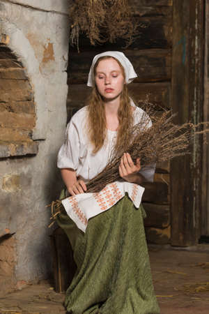 Natural Portrait of Sensual Caucasian Redhaired Girl in Rustic Style Dress Posing With Heather Bouquet in Old House In Front Of the Stove. Vertical Imageの写真素材