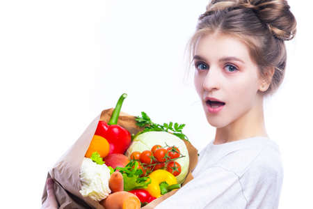 Healthy Eating. Young Surprised Caucasian Girl With Eco Paper Bag Filled With Multiple Vegetables and Groceries Posing Against White Background. Horizontal Image Orientationの写真素材