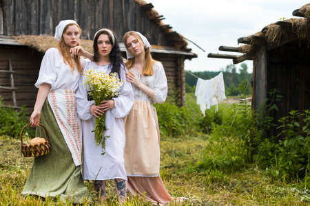 Portrait of Three Lovely Country Girls with Basket of Homemade Bread and Camomiles Posing Together in Village  Outdoor.Horizontal Imageの写真素材