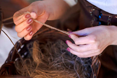 Closeup of Hands of Young Caucasian Woman Spinning Yarn in Retro Dress In Rural Environment....