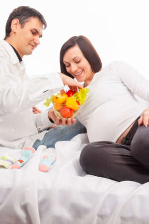 Portrait of Man Offering His Pregnant Wife Fresh Vegetables on Glass Bowl Over White Background....