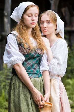 Rural Style Concepts. Two Young Beautful Caucasian Girlfriends in Traditional Rural Outfit  Posing With Caly Jar And Bread Together Outdoor. Vertical Imageの写真素材