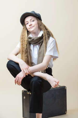Caucasian Teenage Girl in Official Uniform With Suspenders Sitting On Travel Suitcase In Cap And...