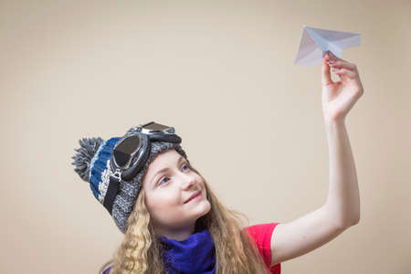 Teenage Girl in Flying Glasses And Knitted Warm Hat Posing With Origami Paper Plane While Sitting on...