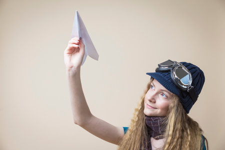 Caucasian Teenager Blond Girl in Flying Gear Launching Origami Paper Plane Over Beige Background. Horizontal Imageの写真素材