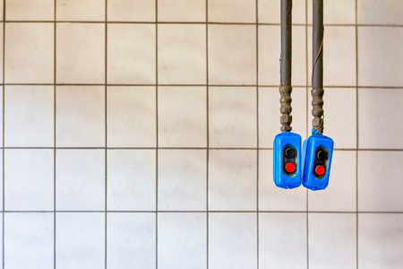 Two Separate Remote Control Panels Hanged On Long Rubber Holders Against White Tiles Wall.Horizontal...
