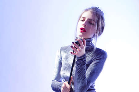 Passionate Singing Caucasian Female In Gray Reflective Dress Posing With Microphone Over White Background. Horizontal Imageの写真素材